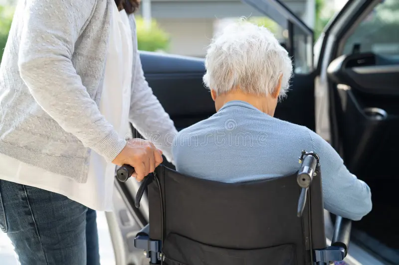 Caregiver assisting senior woman in a wheelchair into a car
